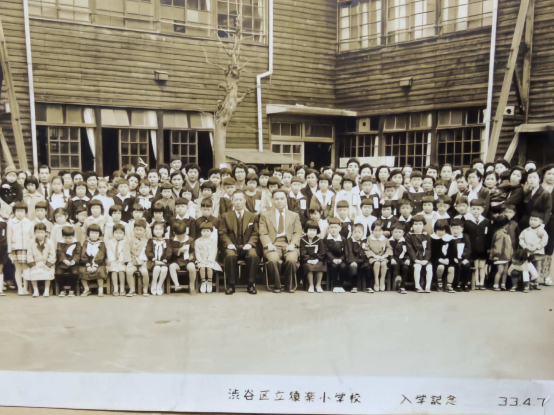 渋谷区立猿楽小学校の校舎前に並ぶ児童と大人の入学記念写真