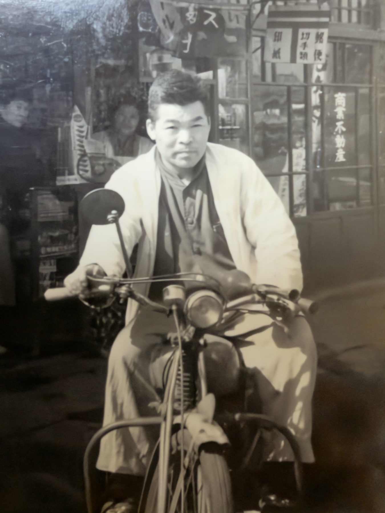 店先で原動機付自転車にまたがる白衣姿の人物